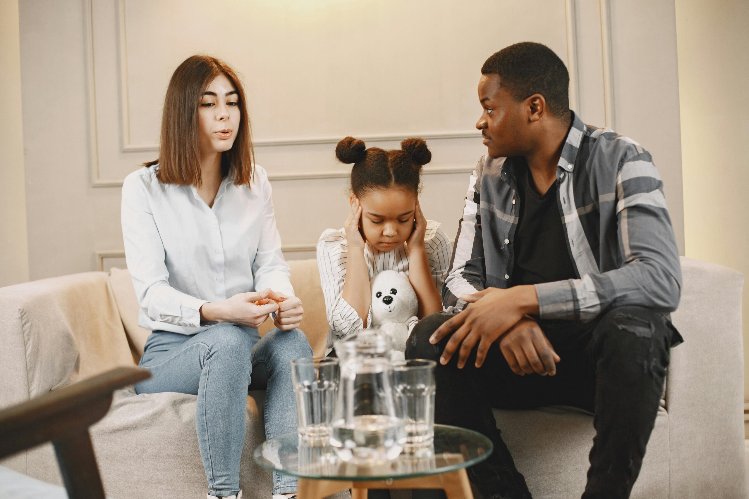Young child covering her ears while sitting on a sofa, representing the emotional impact of custody disputes on children. Custody evaluation in NJ.